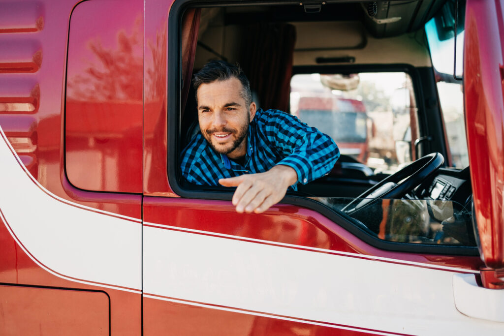 Young handsome bearded man driving his truck and looking through side window. View from outside.